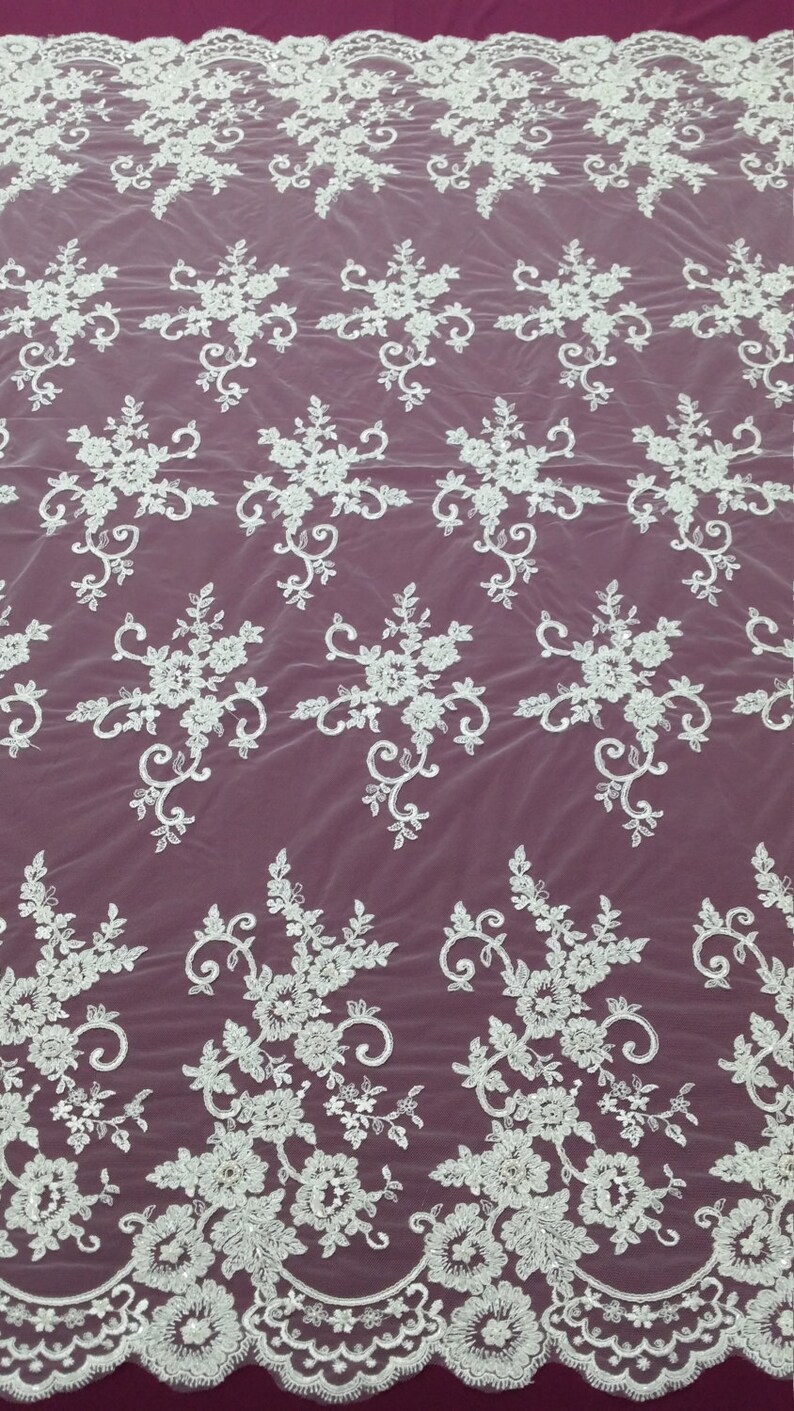 May include: White floral lace fabric with a repeating pattern of flowers and leaves. The lace has a scalloped edge and is set against a burgundy background. This delicate fabric is suitable for bridal wear and other special occasion garments.
