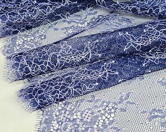 May include: A length of dark navy blue lace fabric featuring a delicate floral pattern with white thread accents. The lace has a scalloped edge with fine, eyelash-like fringe detailing along the border, showcasing a complex, open-weave mesh design.
