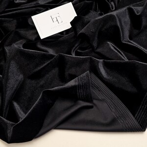 May include: Close-up of black velvet fabric, showing its soft, shiny texture. The fabric is arranged in flowing folds, creating shadows and highlights. A white tag with the text "LOOK TO LUNA" is visible.
