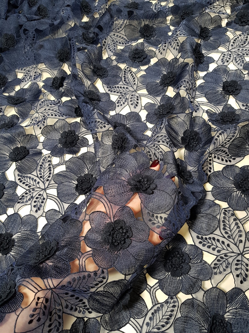 May include: A dark navy blue lace fabric featuring an intricate floral pattern with three-dimensional embroidered flower petals and leaves. The sheer mesh base is covered in dense, layered floral motifs with detailed stitching throughout the design.