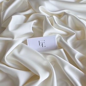 May include: A close-up of a white satin fabric with a small white card that says "Lace to Love" in black text.