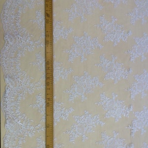 May include: White embroidered lace fabric with a delicate floral pattern. The fabric is shown with a ruler measuring 90 cm.