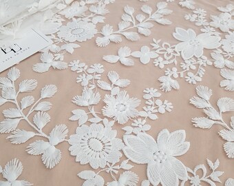 May include: White floral lace fabric featuring a delicate pattern of flowers and leaves. The lace is sheer and has a soft, romantic feel.