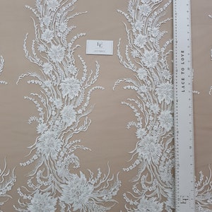 Puede incluir: Tela de encaje floral blanca con un patr&oacute;n delicado. El encaje presenta intrincados dise&ntilde;os florales y un fondo transparente. La tela se mide con una regla en pulgadas.