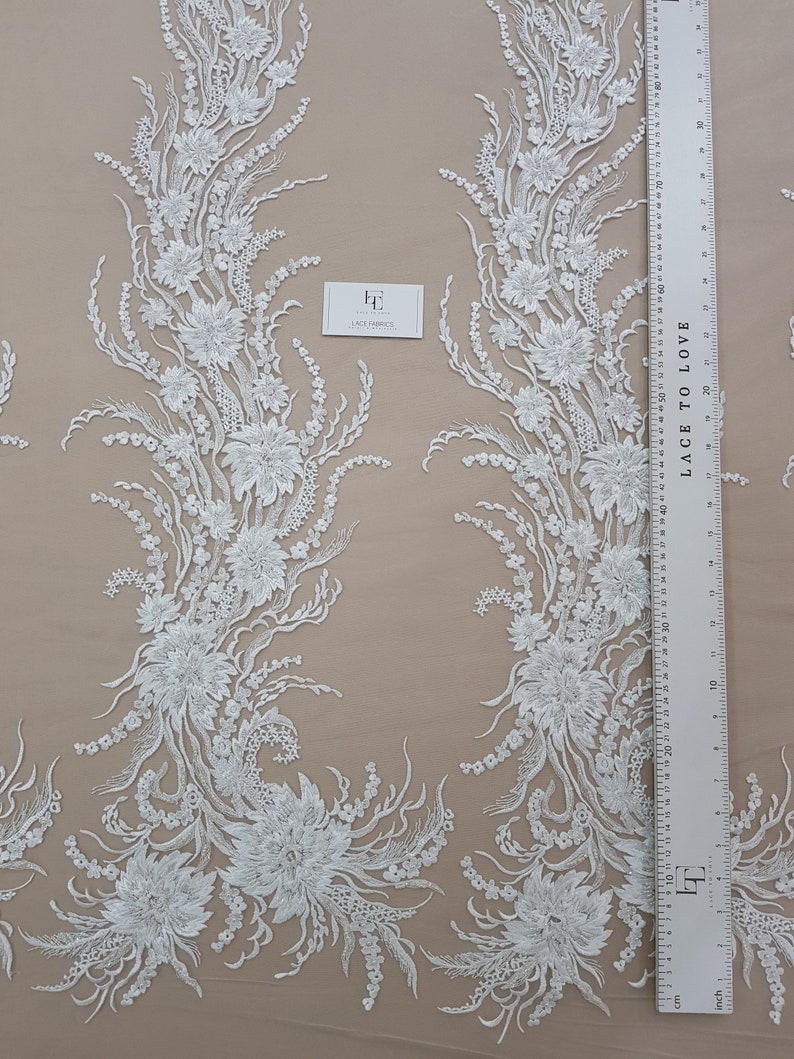 Puede incluir: Tela de encaje floral blanca con un patr&oacute;n delicado. El encaje presenta intrincados dise&ntilde;os florales y un fondo transparente. La tela se mide con una regla en pulgadas.
