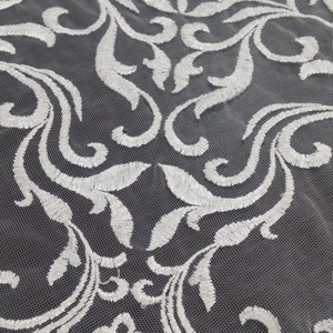 May include: A sheer fabric featuring a white embroidered damask pattern with intricate scrolling leaves and floral motifs. The embroidery is stitched onto a fine, translucent mesh base, creating a repeating symmetrical design across the surface.
