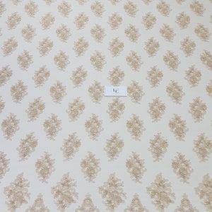 May include: Beige lace fabric with a repeating floral pattern and a scalloped edge. The delicate design features embroidered flowers and small embellishments, creating a textured surface. The fabric is suitable for various craft and design projects.