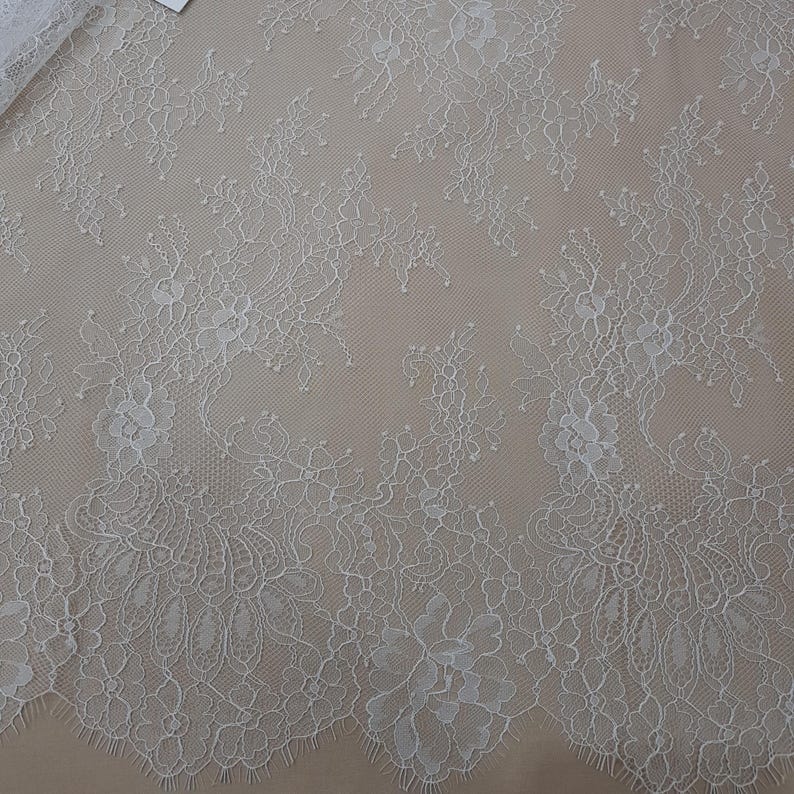 Pode incluir: Tecido de renda marfim com um design floral. A renda apresenta padr&otilde;es detalhados de flores e folhas, criando uma textura delicada e elegante. O tecido &eacute; exibido em um fundo neutro, destacando os detalhes intrincados da renda.