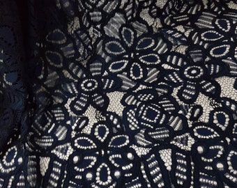 May include: A dark navy blue lace fabric featuring a repeating floral pattern with intricate openwork details and a scalloped edge. The design consists of large, interconnected flower motifs with dense stitching and delicate mesh sections.