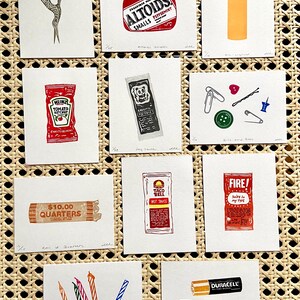Puede incluir: Una colecci&oacute;n de peque&ntilde;as impresiones art&iacute;sticas cuadradas con objetos cotidianos. Las impresiones incluyen unas tijeras, un paquete de Altoids, un encendedor, un sobre de ketchup, un sobre de salsa picante, un rollo de monedas y pilas.