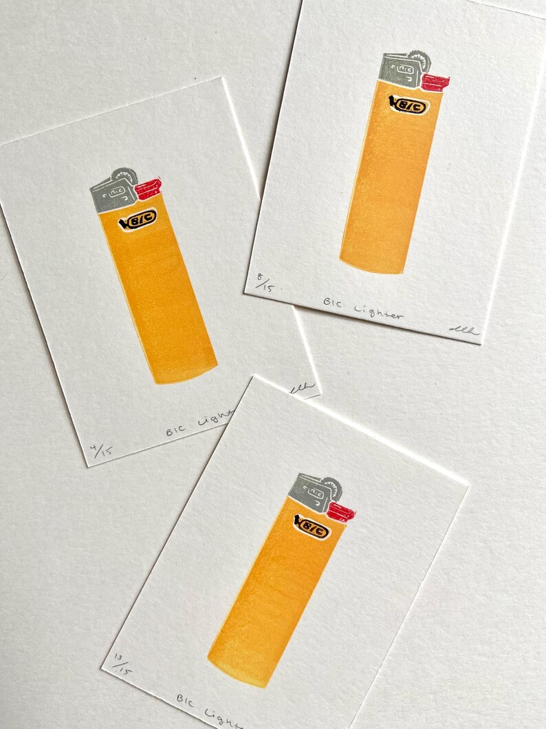 Op de afbeelding: Drie prints van een gele BIC aansteker met grijze en rode accenten op wit papier. De tekst "BIC Lighter" en een breuk van 15 staan onderaan elke print.