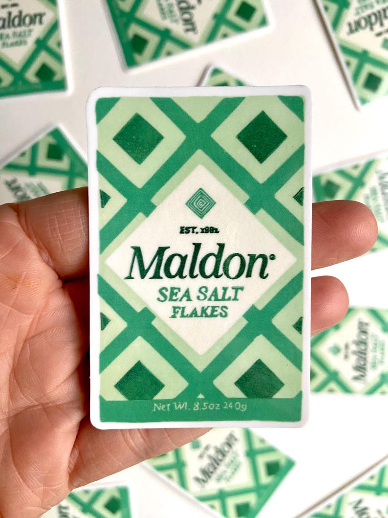 Może przedstawiać: Naklejka z zielono-białym geometrycznym wzorem, z napisem "Maldon Sea Salt Flakes". Naklejka zawiera tekst "Waga netto 240g". Marka "Maldon" jest pogrubiona, z rokiem "EST. 1982".