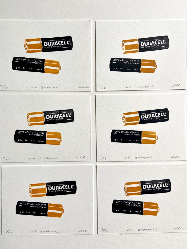 Puede incluir: Una serie de seis grabados art&iacute;sticos con pilas AA Duracell. Cada grabado muestra dos pilas, una con el logotipo de Duracell y la otra con texto. Los grabados est&aacute;n numerados 3/10 y 7/10, con el texto "AA Batteries" debajo.