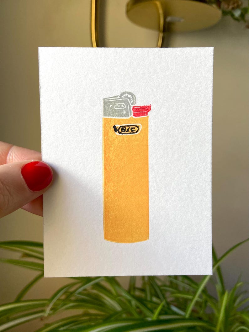 Op de afbeelding: Handgeschilderde illustratie van een gele BIC-aansteker op wit papier. De aansteker heeft een zilveren bovenkant en een rode veiligheidsklep. Het BIC-logo is zichtbaar op de voorkant van de aansteker.
