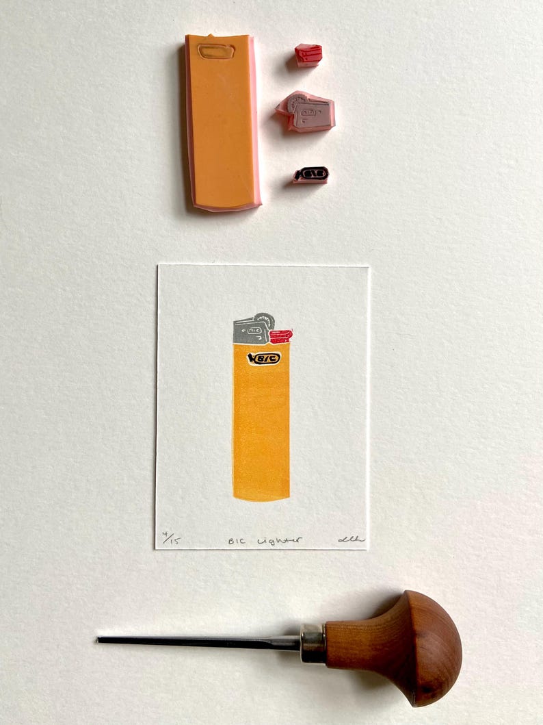 Op de afbeelding: Een print van een gele BIC-aansteker met de tekst "BIC Lighter" en het nummer "4/15". De afbeelding bevat ook een snijgereedschap en diverse rubberen stempels.