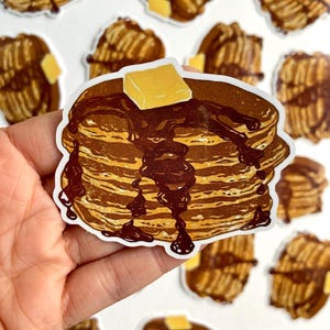 May include: A stack of pancakes with chocolate syrup and a pat of butter. The pancakes are brown and the syrup is dark brown. The butter is yellow. The pancakes are on a white background.