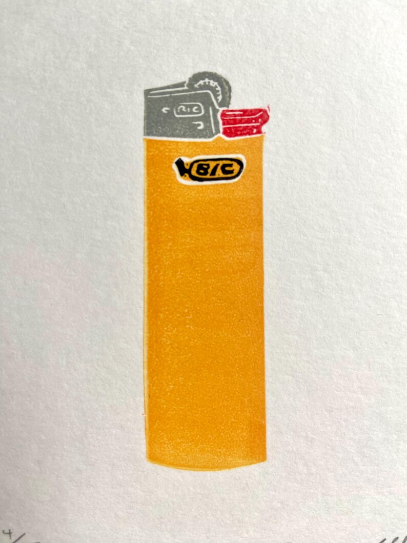 Op de afbeelding: Een print van een gele BIC-aansteker met een grijze bovenkant en rode accenten. Het BIC-logo is zichtbaar op de voorkant. De aansteker staat tegen een witte achtergrond.