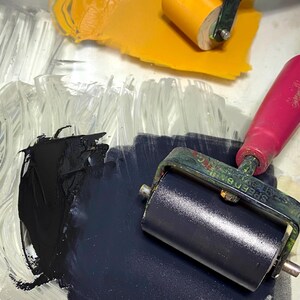 Puede incluir: Primer plano de una paleta transparente con pintura amarilla y azul oscuro. Dos rodillos Speedball con mangos rosas est&aacute;n colocados en la paleta. Ideal para proyectos art&iacute;sticos.