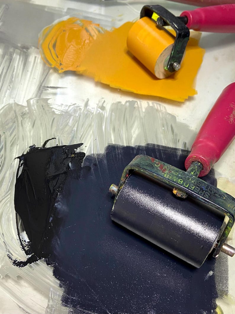 Puede incluir: Primer plano de una paleta transparente con pintura amarilla y azul oscuro. Dos rodillos Speedball con mangos rosas est&aacute;n colocados en la paleta. Ideal para proyectos art&iacute;sticos.