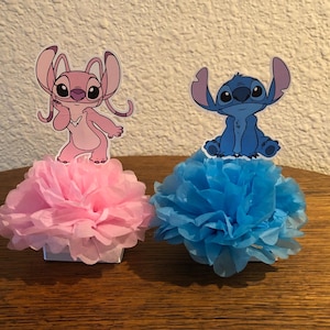 Puede incluir: Dos centros de mesa decorativos con personajes de dibujos animados. Uno tiene una base de pomp&oacute;n rosa con un personaje rosa, el otro tiene una base de pomp&oacute;n azul con un personaje azul. Los personajes son de una pel&iacute;cula de animaci&oacute;n popular.