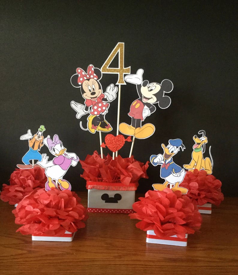 May include: Mickey Mouse and Minnie Mouse themed centerpiece with red tissue paper balls, a red heart, and a gold glitter number 4. The centerpiece is surrounded by four smaller centerpieces featuring Donald Duck, Goofy, Pluto, and Daisy Duck.