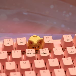 K&ouml;nnte beinhalten: Eine rosa Tastatur mit einer gelben Hundetastenkappe. Die Tastatur hat Tasten mit den Beschriftungen F5, FG, F8, F9, GA, 7, Y, U, H, J, K, L, P, O, 9, 0 und -. Der Text '@sentimentaldolliez' ist auf der Tastatur sichtbar.