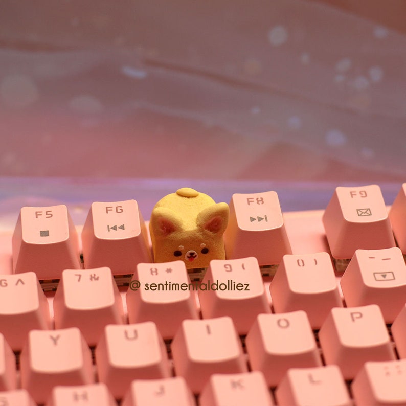 K&ouml;nnte beinhalten: Eine rosa Tastatur mit einer gelben Hundetastenkappe. Die Tastatur hat Tasten mit den Beschriftungen F5, FG, F8, F9, GA, 7, Y, U, H, J, K, L, P, O, 9, 0 und -. Der Text '@sentimentaldolliez' ist auf der Tastatur sichtbar.