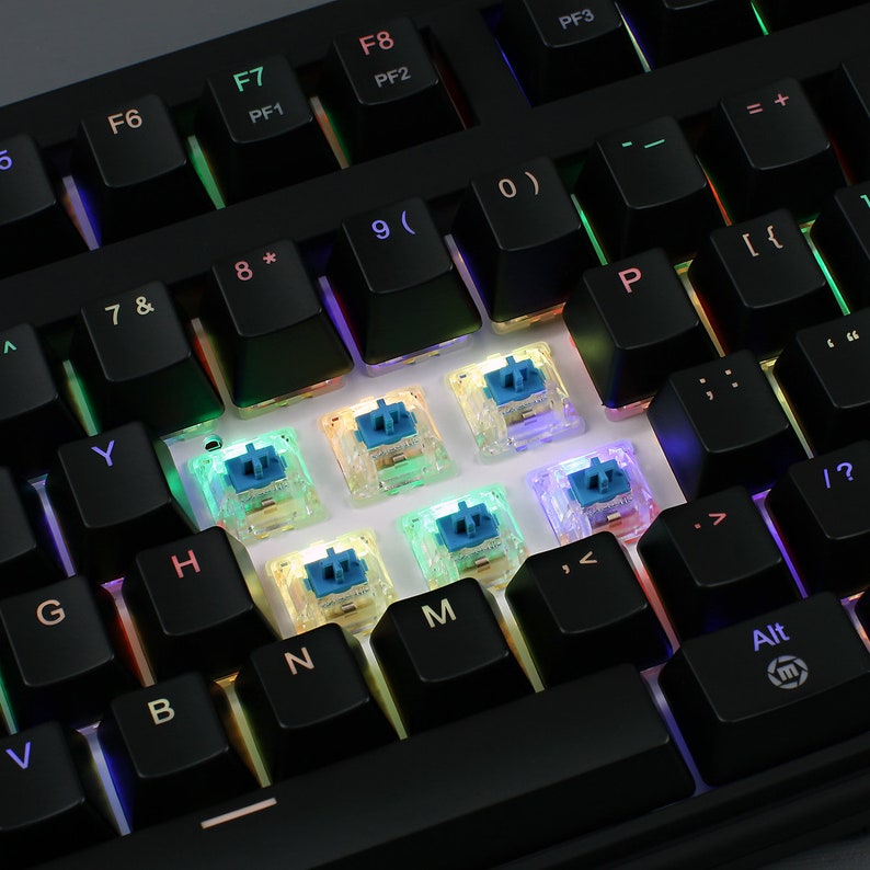 K&ouml;nnte beinhalten: Nahaufnahme einer schwarzen mechanischen Tastatur mit beleuchteten Tasten. Die schwarzen Tastenkappen sind sichtbar, und einige Tasten sind entfernt, wodurch blaue Schalter freigelegt werden. Die Tastatur verf&uuml;gt &uuml;ber verschiedene Funktionstasten und Symbole.