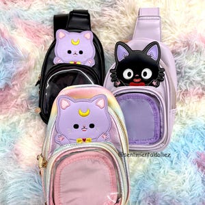 K&ouml;nnte beinhalten: Drei kleine, transparente, durchsichtige Umh&auml;ngetaschen mit Rei&szlig;verschluss. Die Taschen haben eine transparente Fronttasche und eine kleinere, undurchsichtige R&uuml;ckentasche. Die Taschen zeigen verschiedene Comicfiguren: eine schwarze Katze, eine lila Katze mit einem Halbmond und eine lila Katze mit einem Halbmond und einem Regenbogenhintergrund.