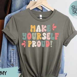 May include: Army green t-shirt with a colourful retro font graphic that says "Make Yourself Proud!" The shirt is made of a soft, comfortable fabric.