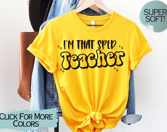 Könnte beinhalten: Gelbes T-Shirt mit kurzen Ärmeln und dem Text "I'm That SPED Teacher" in Schwarz, mit einer Retro-Schriftart. Das Shirt hängt an einem Kleiderbügel und hat einen geknoteten Saum.