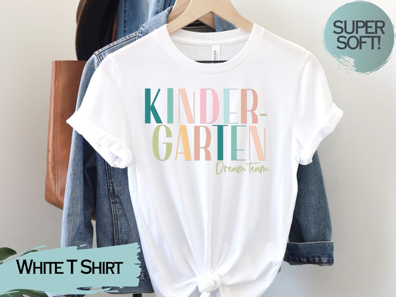May include: White t-shirt with the text "KINDERGARTEN Dream Team" in colorful block letters. The letters are in shades of pink, green, yellow, and orange.
