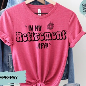 Op de afbeelding: Een roze T-shirt met de tekst "In My Retirement Era!" in zwart, met een discobal-afbeelding boven de tekst. Het shirt is gemaakt van een zacht, comfortabel materiaal.