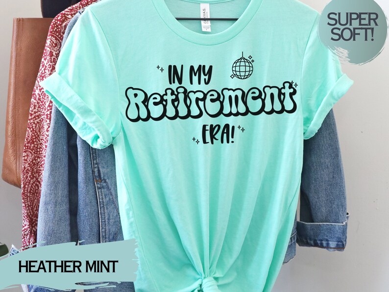 Op de afbeelding: Een heide mintgroen t-shirt met de tekst "In My Retirement Era!" in zwart, met een discobal-afbeelding boven de tekst. De tekst is in een retro-lettertype stijl.