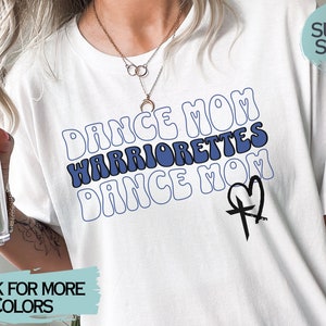 Puede incluir: Camiseta blanca con texto azul y blanco que dice "Dance Mom Warriorrettes Dance Mom" con un gr&aacute;fico de cruz y coraz&oacute;n negro. El texto est&aacute; en una fuente retro.
