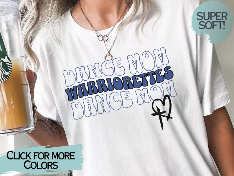 Puede incluir: Camiseta blanca con texto azul y blanco que dice "Dance Mom Warriorrettes Dance Mom" con un gr&aacute;fico de cruz y coraz&oacute;n negro. El texto est&aacute; en una fuente retro.