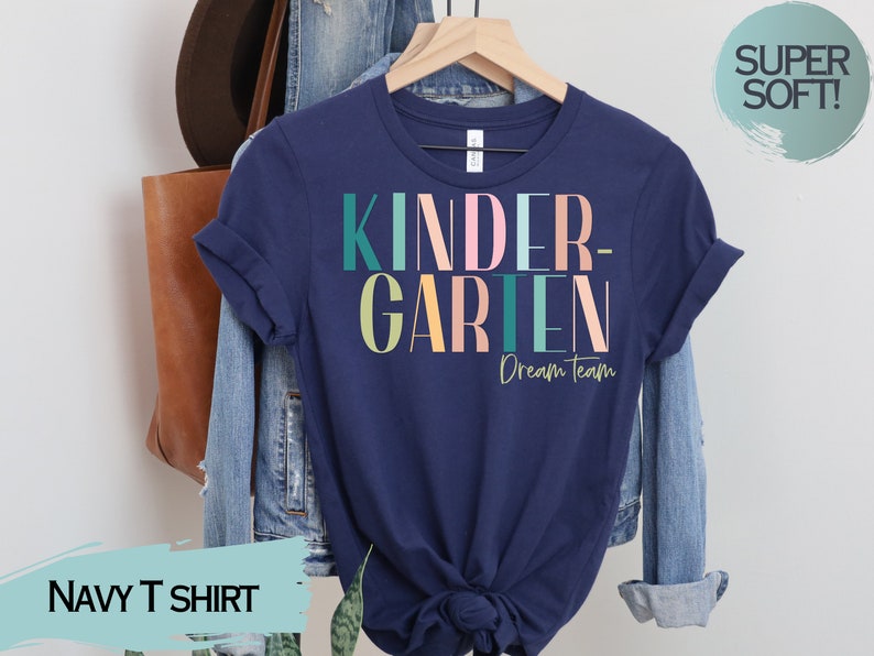 May include: Navy blue t-shirt with the text "KINDERGARTEN - Dream Team" in colorful letters. The shirt is made of a soft, comfortable material.