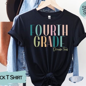 May include: Black t-shirt with the text "FOURTH GRADE Dream Team" in colorful letters. The shirt is on a hanger and has a "SUPER SOFT!" tag.