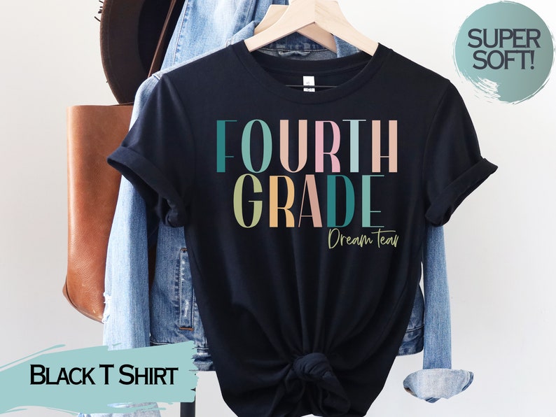 May include: Black t-shirt with the text "FOURTH GRADE Dream Team" in colorful letters. The shirt is on a hanger and has a "SUPER SOFT!" tag.