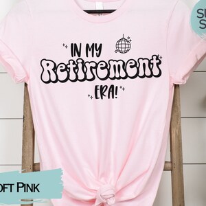 Op de afbeelding: Een zacht roze T-shirt met de tekst "In My Retirement Era!" in zwart, met een discobal-afbeelding boven de tekst.
