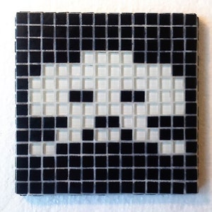 Op de afbeelding: Vierkante mozaïektegel met een gepixeld alien-ontwerp in zwart en wit. Het ontwerp bestaat uit kleine, vierkante tegels, wat een retro, videogame-achtige uitstraling geeft. De tegel is vierkant van vorm.