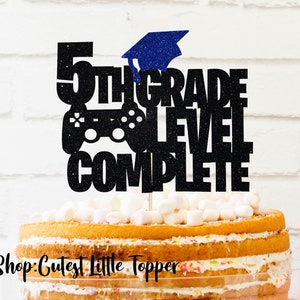 May include: Black glitter cake topper with a graduation cap, a video game controller, and the text "5th Grade Level Complete".