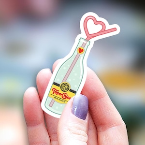 May include: A sticker of a green glass bottle with a pink heart-shaped straw. The bottle has a yellow label with the text "Topo Chico" and "Sparkling Mineral Water".