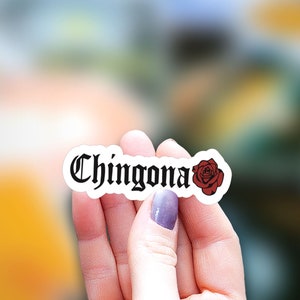Pu&ograve; includere: Un adesivo bianco con la parola "Chingona" in caratteri gotici neri e una grafica di rosa rossa.