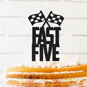 May include: Black and white checkered flags with the words "Fast Five" on a layered cake with white frosting and sprinkles.