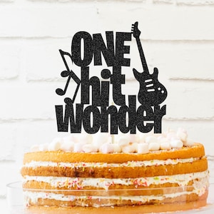 May include: Black glitter cake topper with the text "One Hit Wonder" and a guitar graphic.