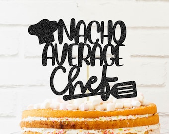 May include: Black glitter cake topper with the text "Nacho Average Chef" and a chef's hat and spatula. The topper is on a multi-layered cake with white frosting and sprinkles.