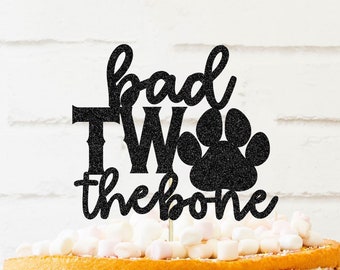 May include: Black glitter cake topper with the text "bad two the bone" and a paw print.