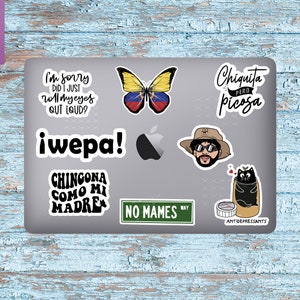May include: A laptop computer covered in stickers. The stickers feature a butterfly with the colors of the Venezuelan flag, a cartoon character with sunglasses and a hat, a black cat in a pill bottle, and various text-based stickers with phrases in Spanish.