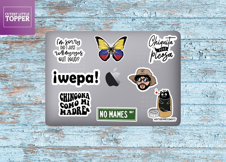 May include: A laptop computer covered in stickers. The stickers feature a butterfly with the colors of the Venezuelan flag, a cartoon character with sunglasses and a hat, a black cat in a pill bottle, and various text-based stickers with phrases in Spanish.